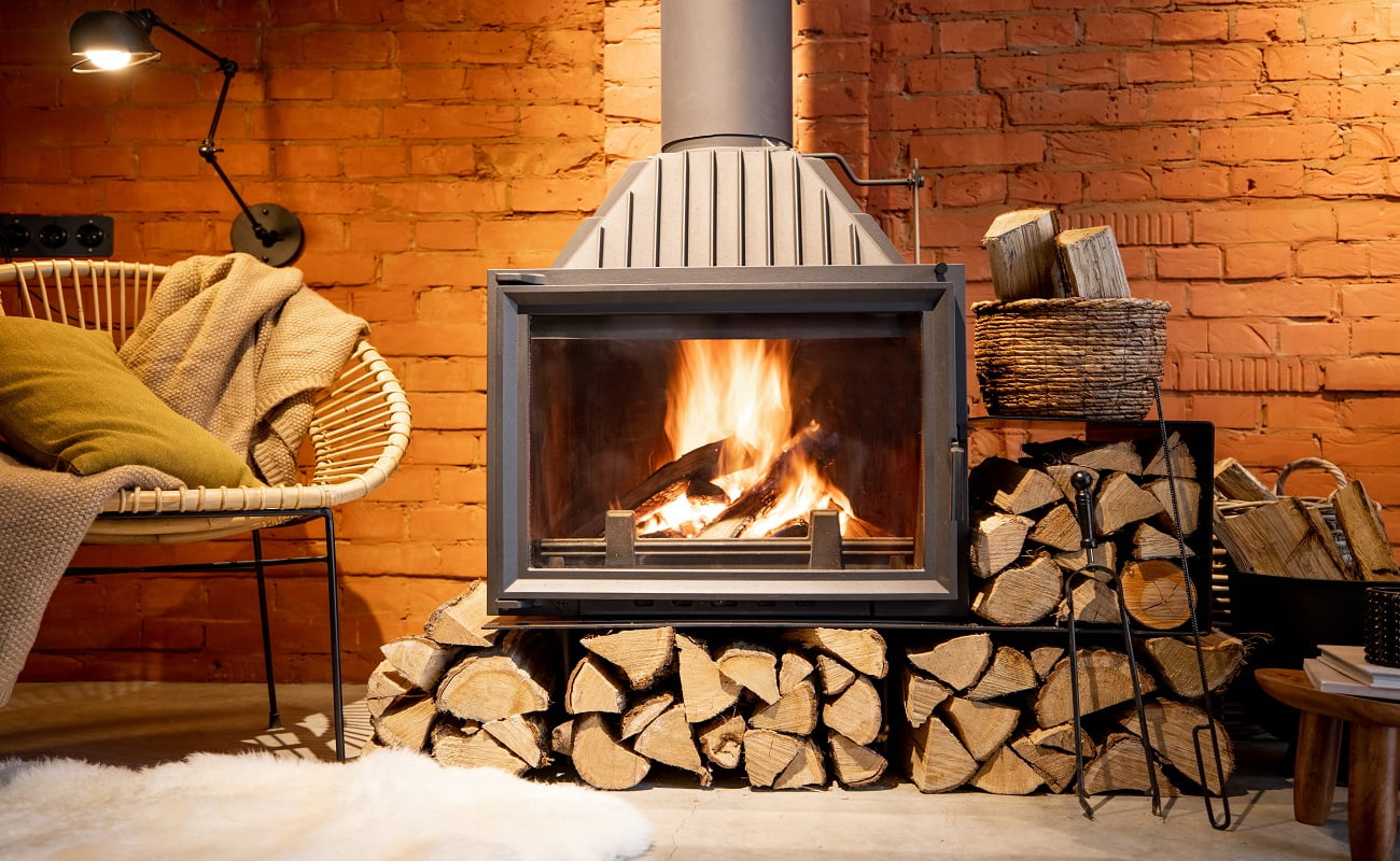Cozy fireplace with firewood in the loft style home interior with brick wall background, burning fire in the fireplace, house coziness in winter